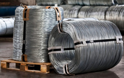 Two large rolls of galvanized steel wire with one in its side in front of several more rolls.