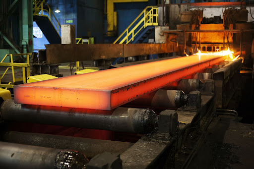 A slab of hot steel rolls through a production facility.